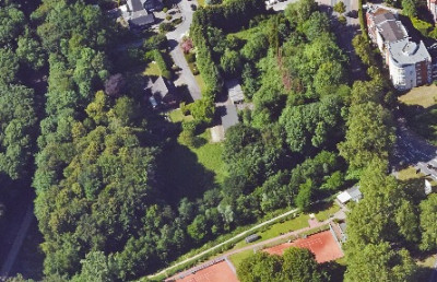 Luftaufnahme eines Stadtgebiets mit Häusern, Bäumen, einem Asche-Sportplatz und Fußwegen
