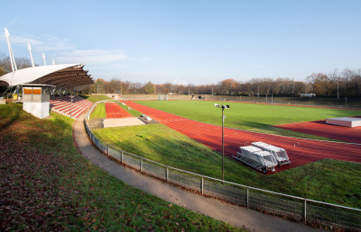 Eine Sportbahn mit Grünfläche, die Tribüne links im Bild